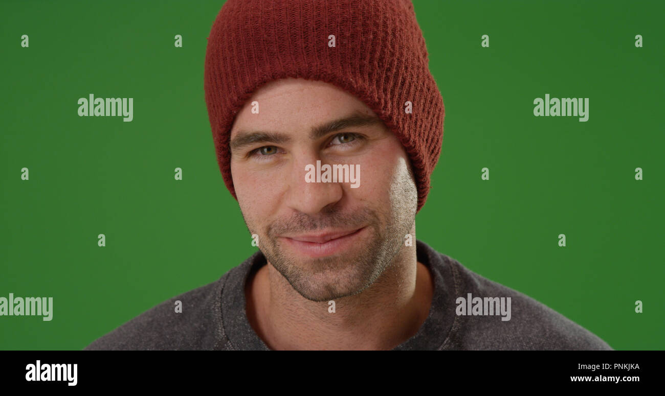 Charming young man wearing beanie smiling at camera on green screen Stock Photo