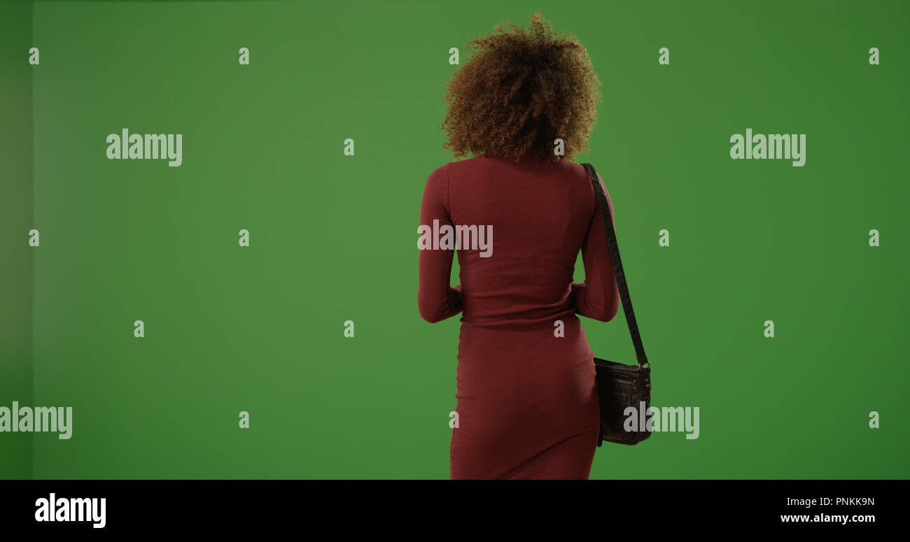 Young black woman in dress standing with back to camera on green screen ...