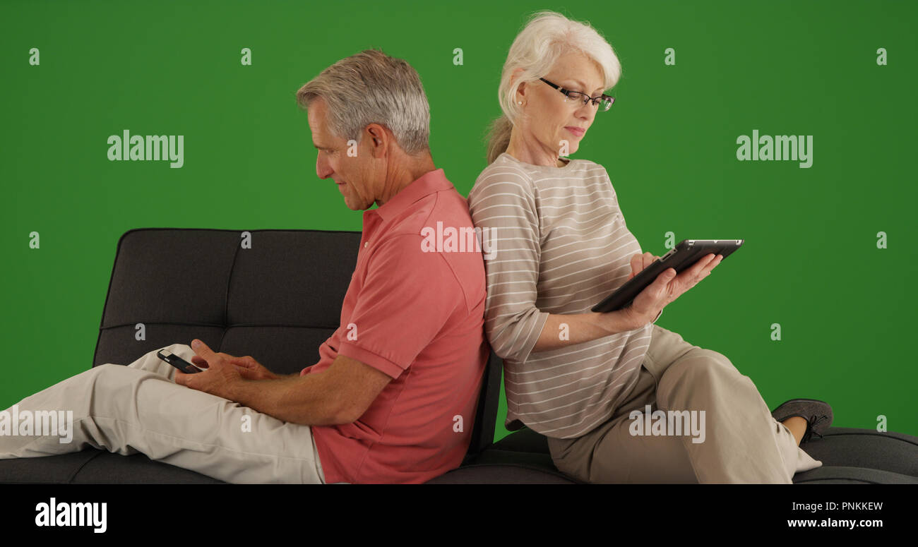 Senior couple using devices on couch at home on green screen Stock Photo