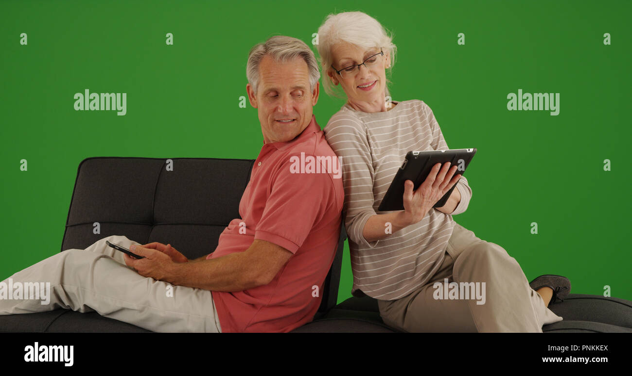 Senior couple sitting on couch using technology on green screen Stock Photo