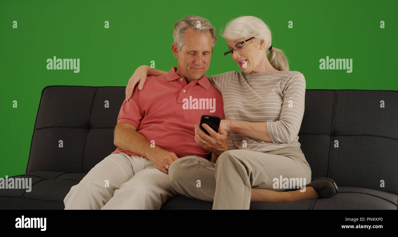 Elderly couple sitting on couch using smartphone on green screen Stock Photo