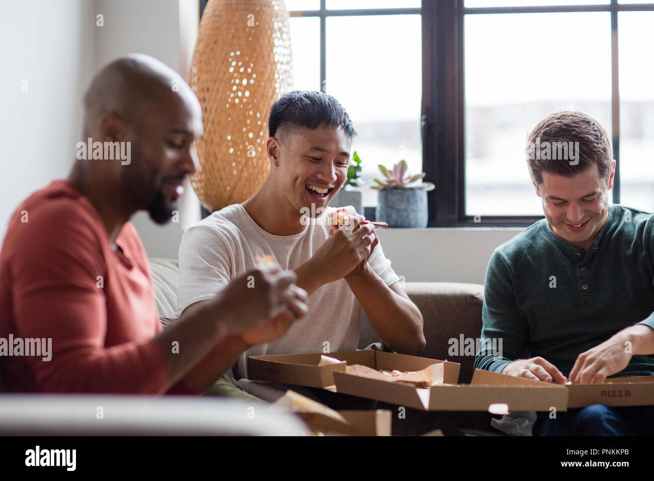 Male friends eating takeout pizza in an apartment Stock Photo