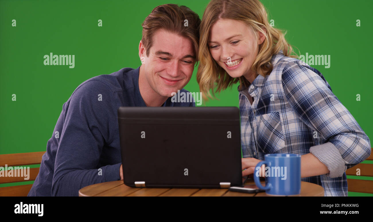 Portrait of millennial man and woman watching video on laptop on green ...