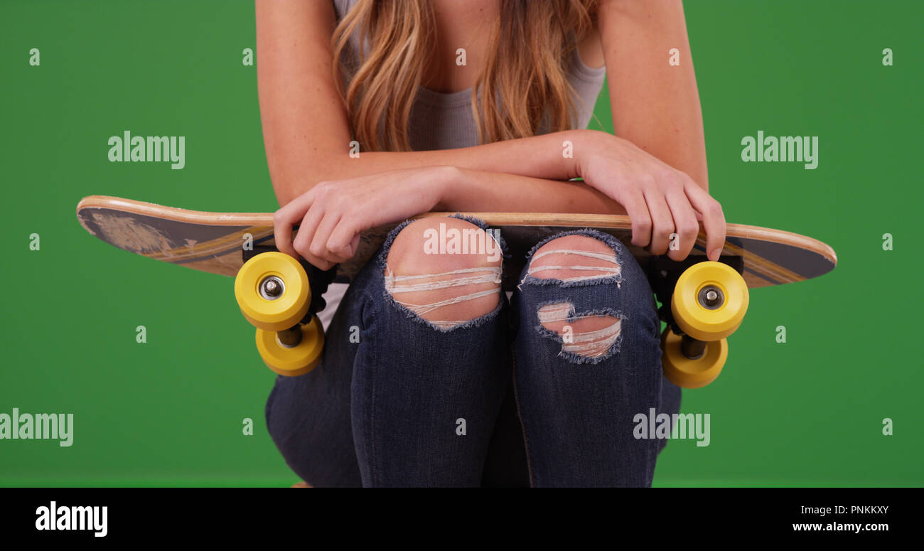Young white female wearing ripped jeans with skateboard on green screen