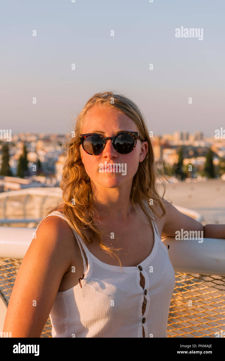 Young woman with white top and sunglasses looks into the camera, Plaza de la Encarnacion, behind houses, Seville, Andalusia Stock Photo