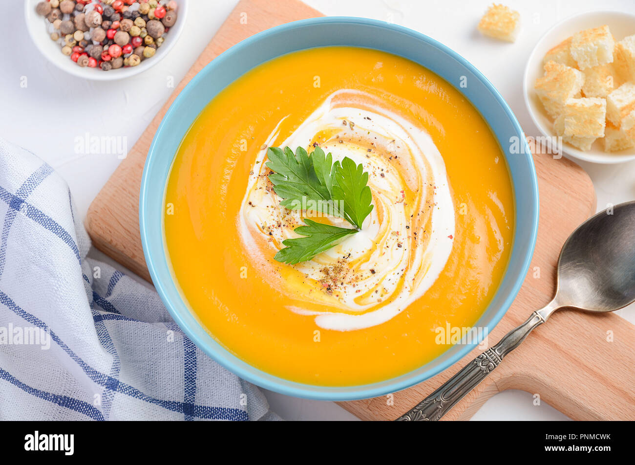 Pumpkin soup with cream and parsley on white table. Stock Photo