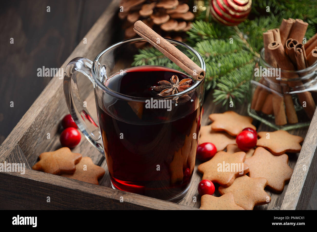 Christmas mulled wine. Holiday concept decorated with Fir branches, Gingerbread Cookies and Cranberries on dark wooden tray. Stock Photo