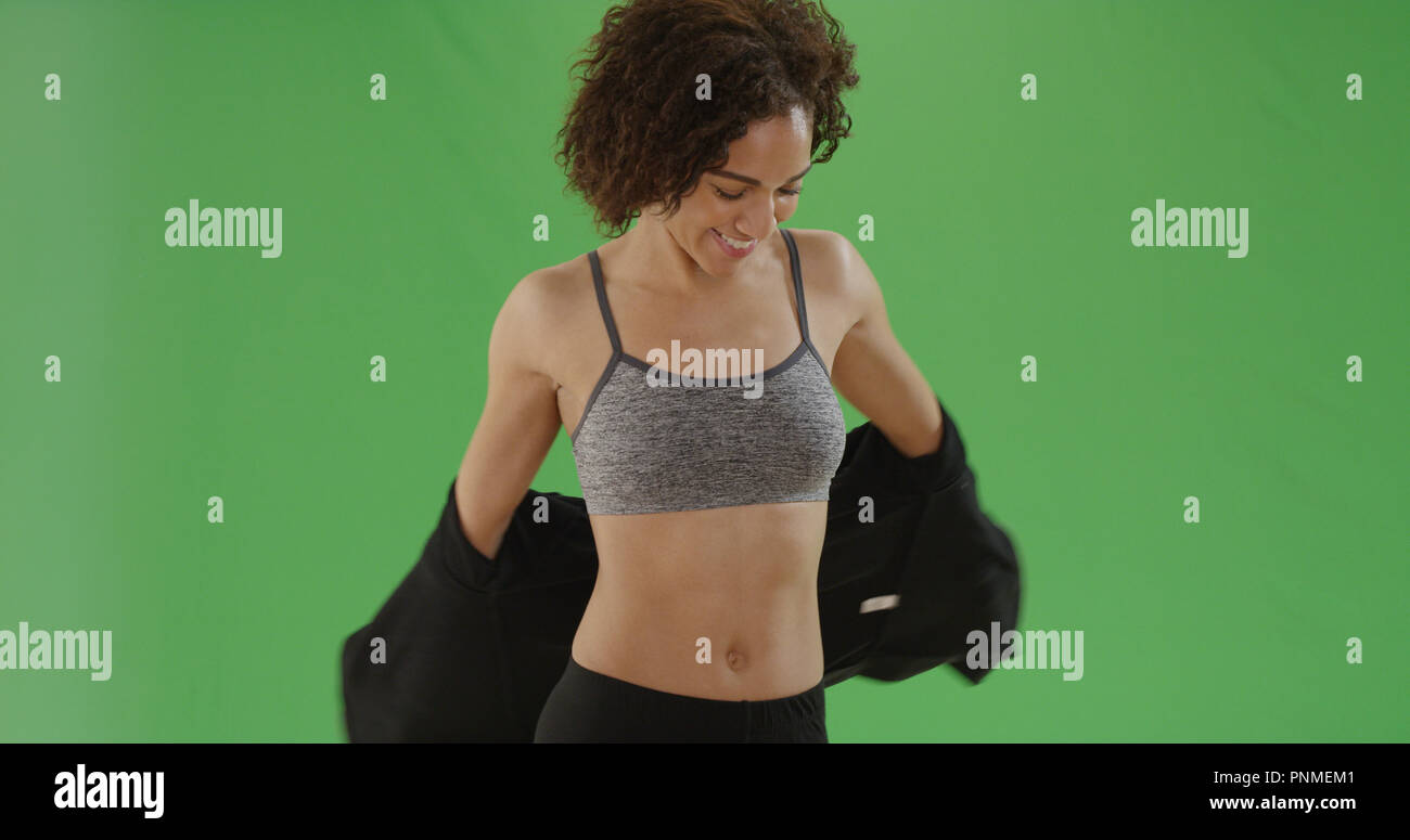Young fit black girl in sports bra takes her jacket off on green
