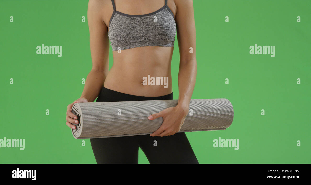Slender black girl in sports bra holds her yoga mat on green screen