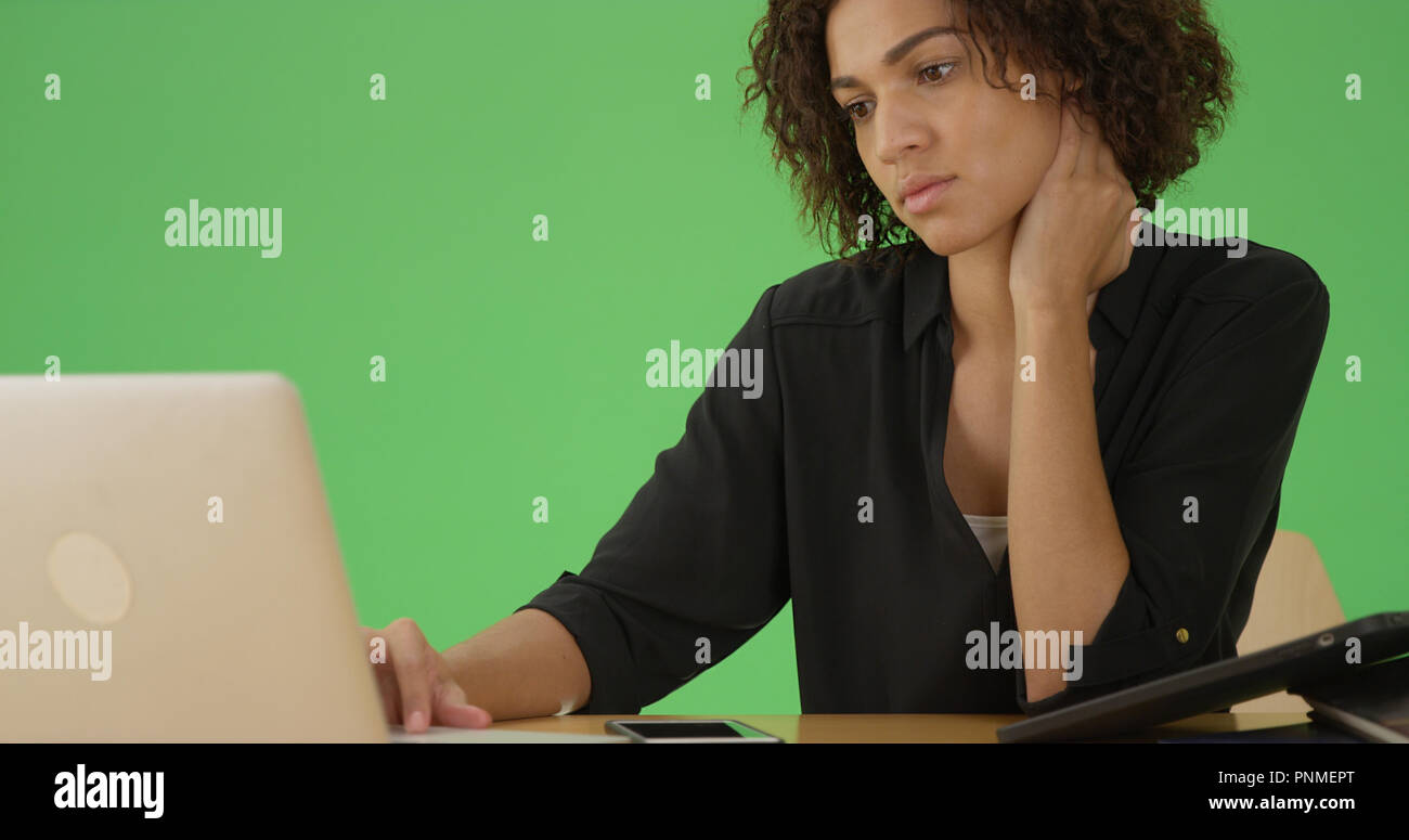 A young african American woman uses her laptop at her desk on green ...
