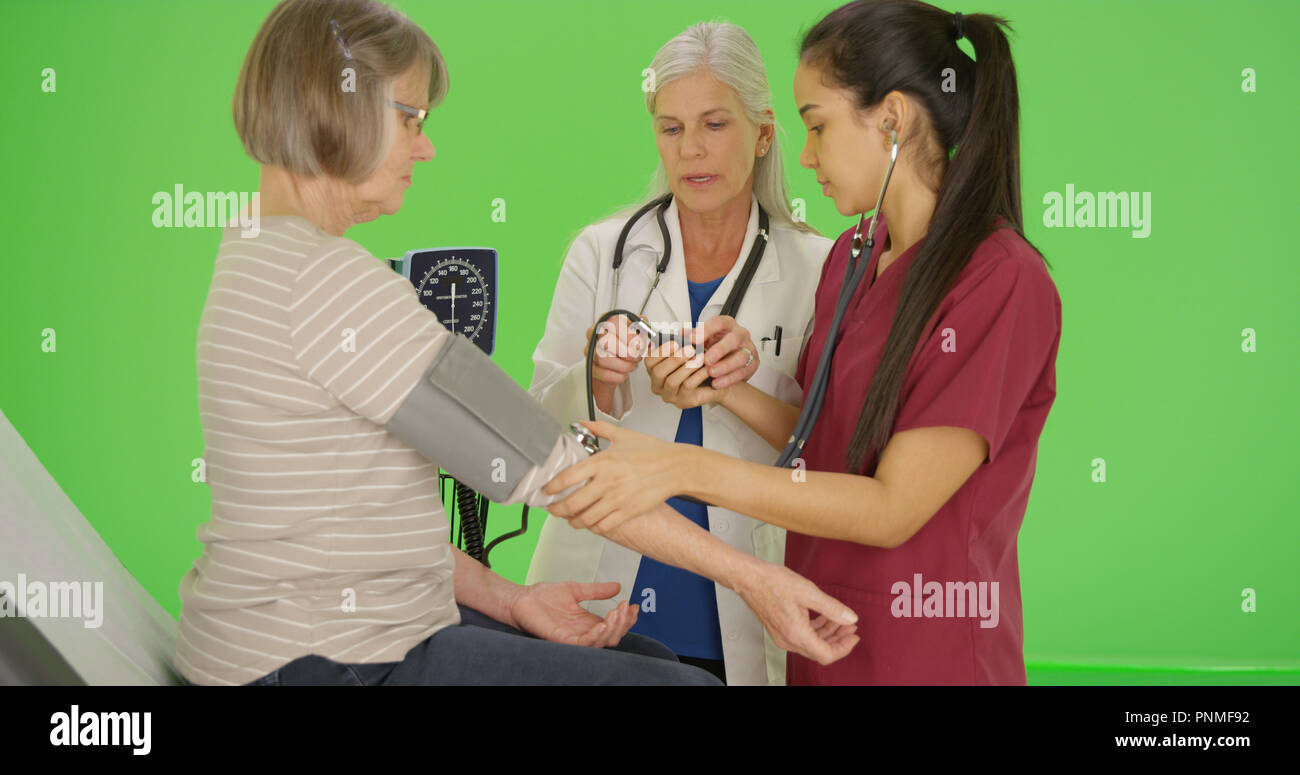 Female doctor teaching student nurse to take blood pressure green screen Stock Photo