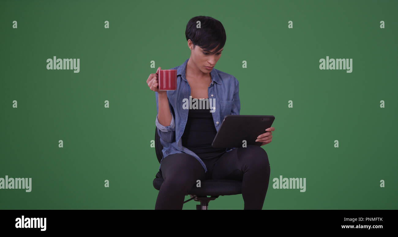 Black woman in an office chair reading on her tablet on green screen Stock Photo