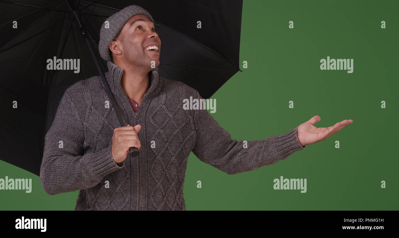 An African American man with umbrella enjoying the rain on green screen ...