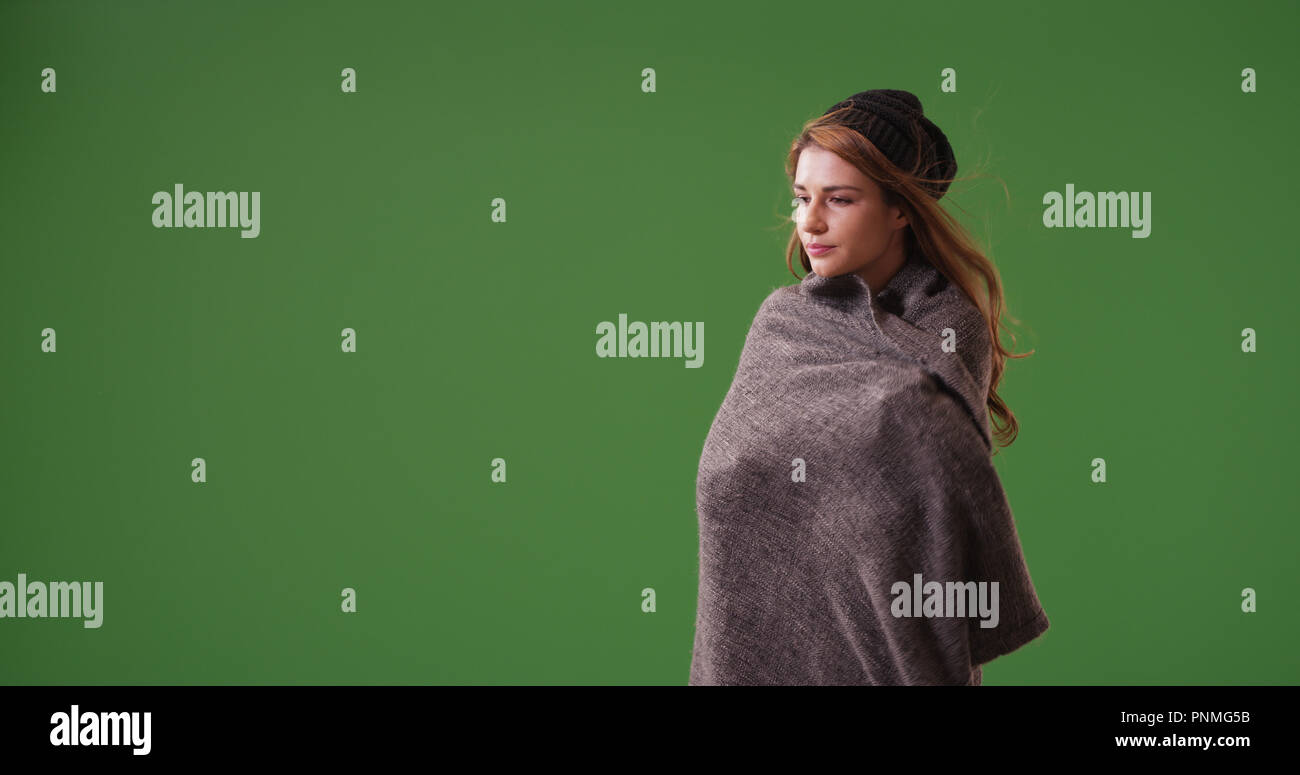 Young woman wrapped up in blanket standing on green screen Stock Photo