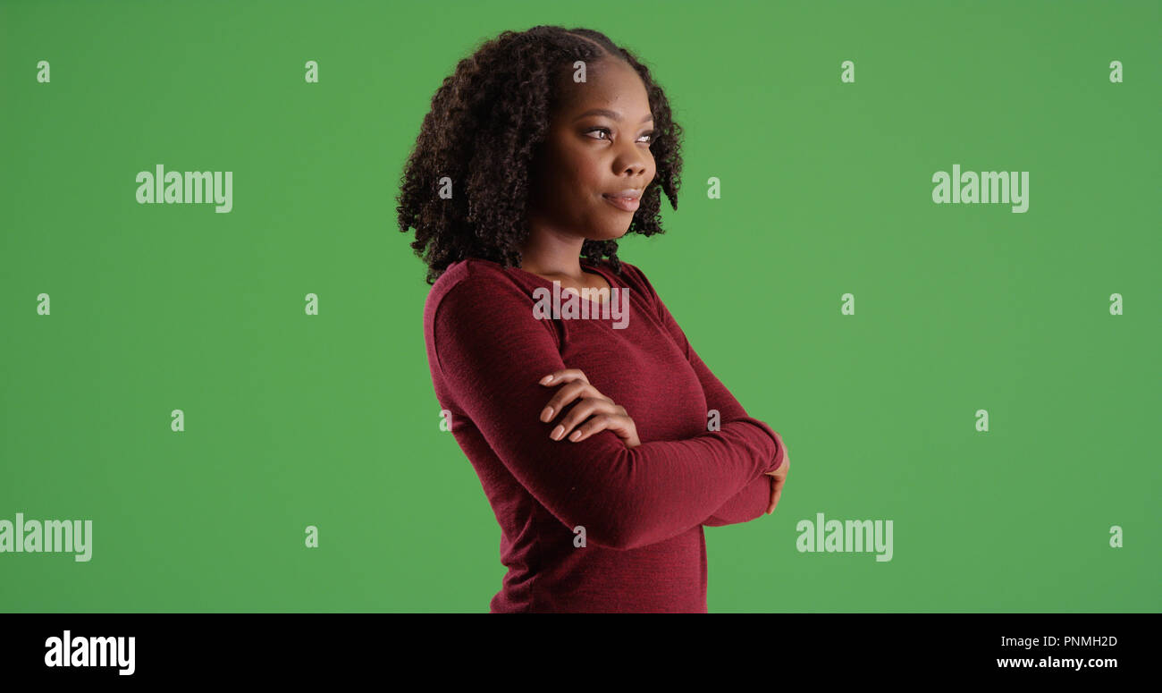 Young black woman standing with arms crossed looking offscreen on green ...