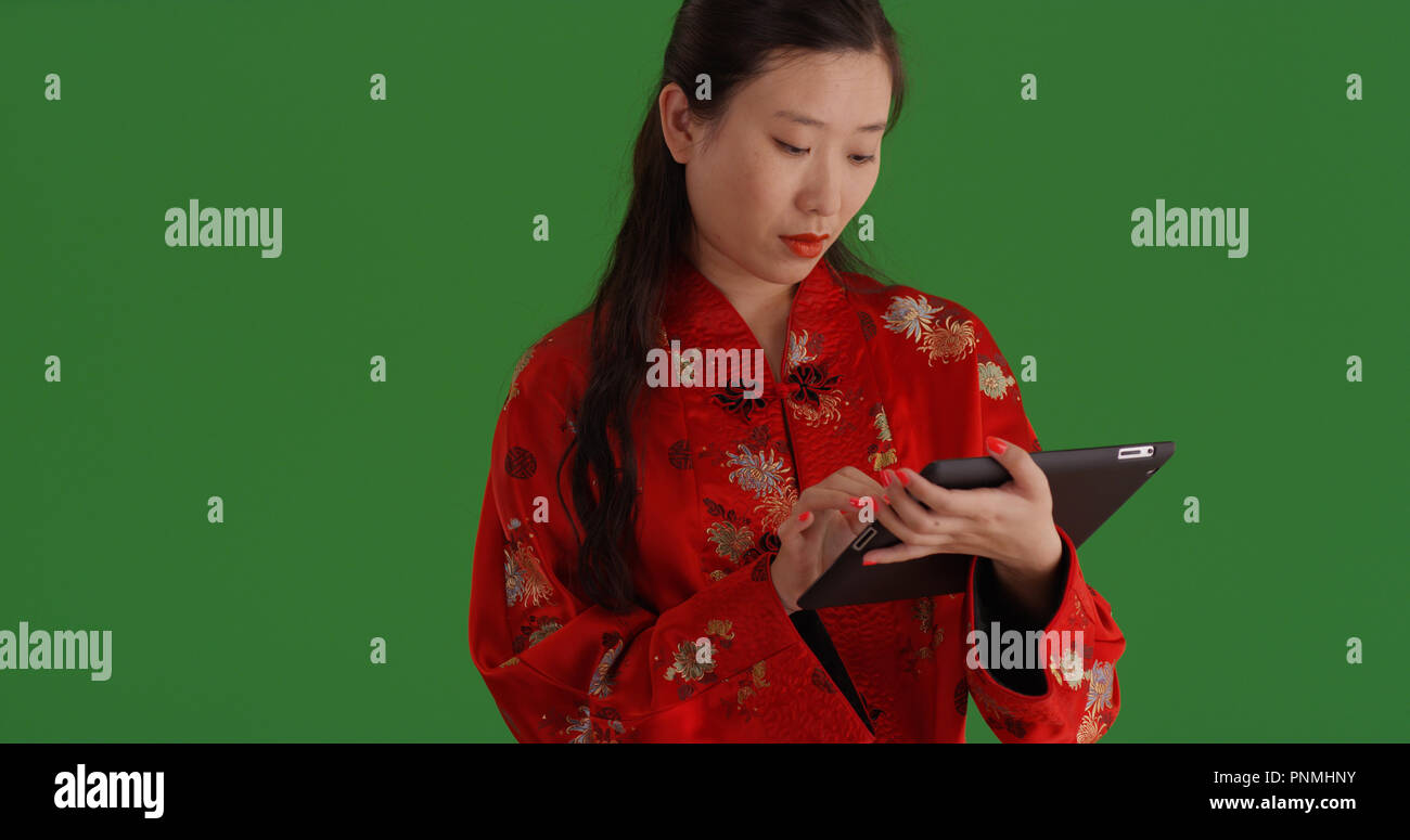 Asian woman in traditional clothes using tablet device on green screen Stock Photo