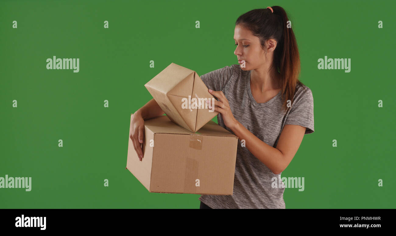 Young lady carrying cardboard boxes reading shipping label on green
