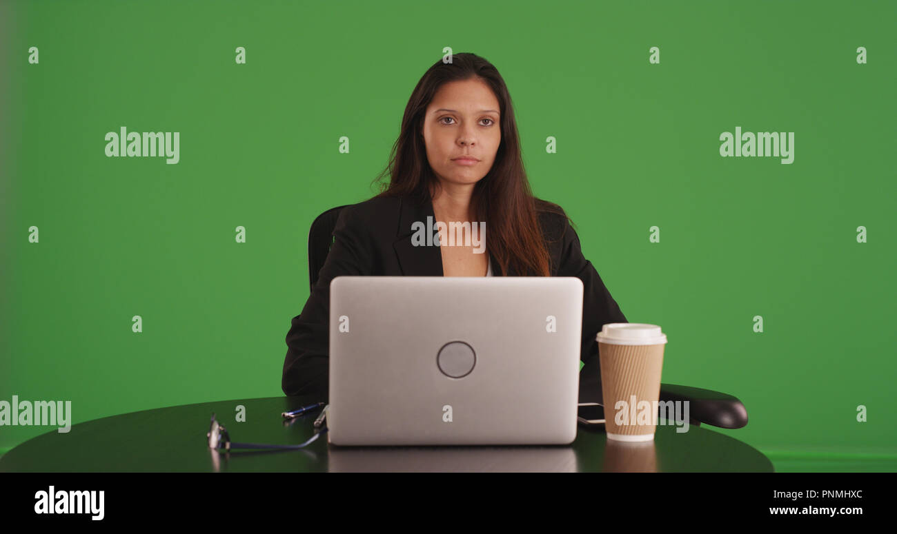 Young businesswoman sitting at table with laptop computer on green screen Stock Photo