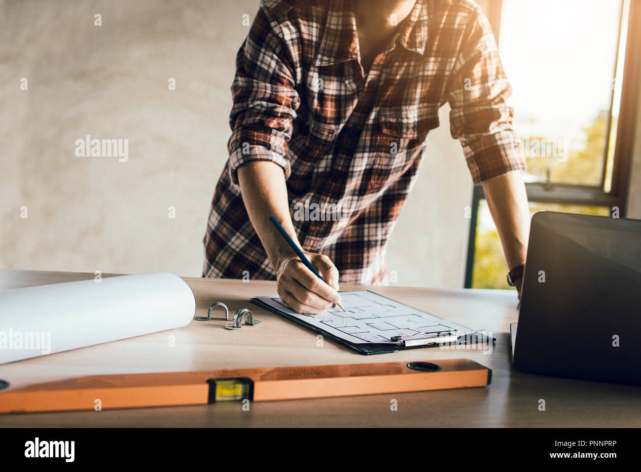 Man working, engineering checking, writing on blueprint and looking on laptop at site construction work. Stock Photo
