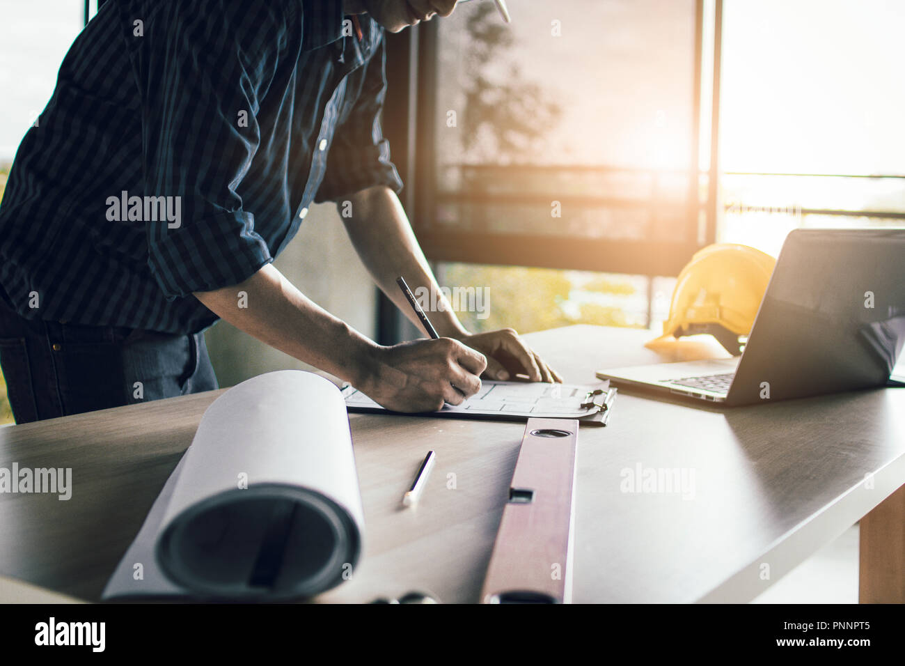 Man working, engineering checking, writing on blueprint and looking on laptop at site construction work. Stock Photo