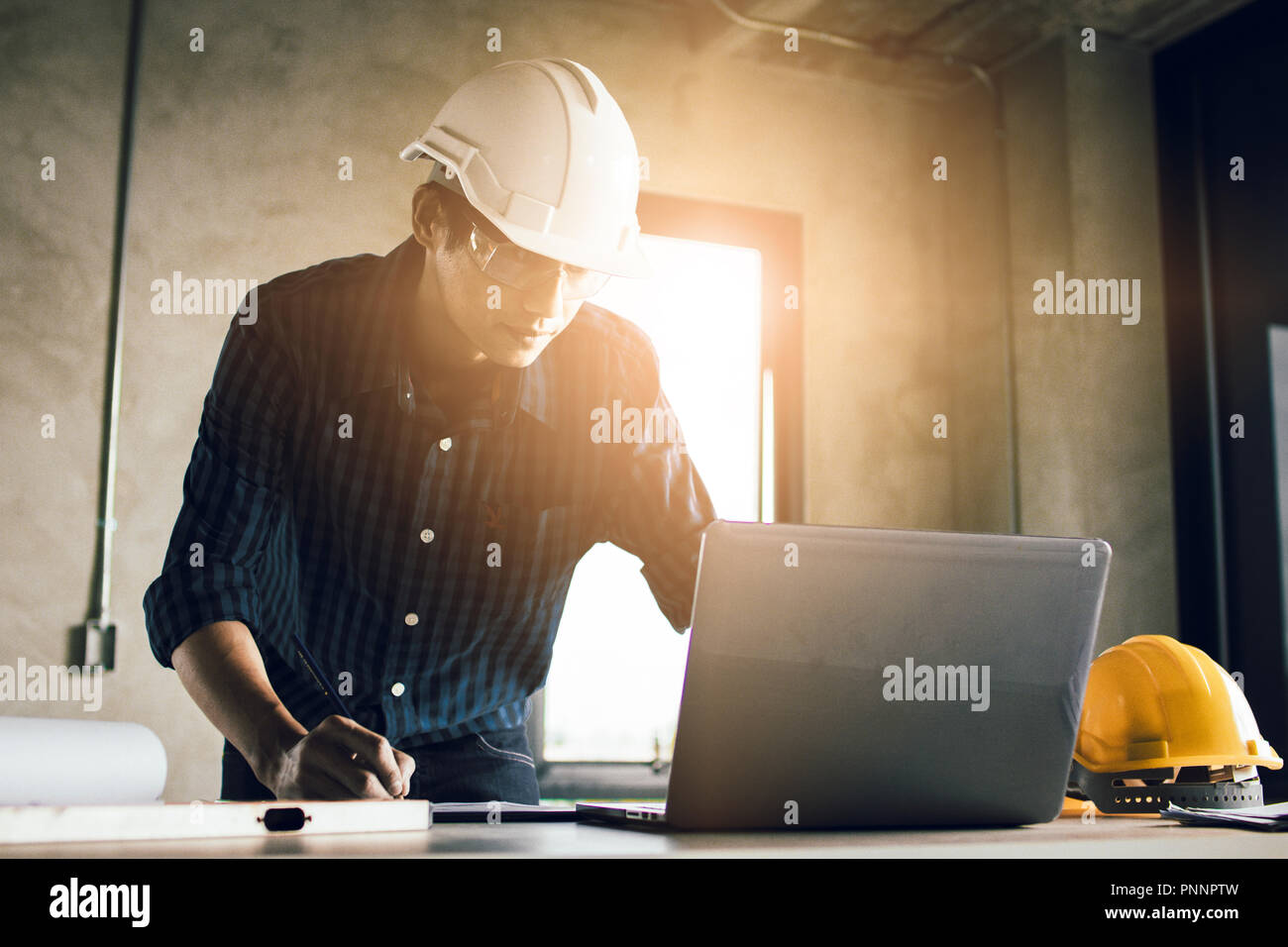 Man working, engineering checking, writing on blueprint and looking on laptop at site construction work. Stock Photo