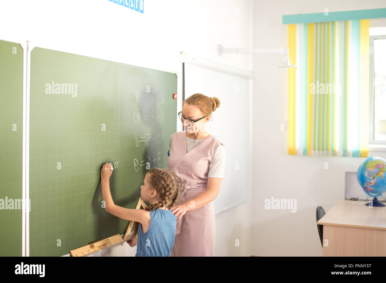 Schoolchild with teacher in classroom. Girl near chalkboard show her homework Stock Photo