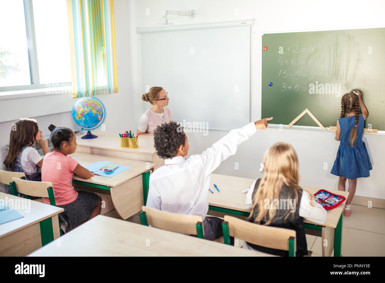 Schoolchild with teacher in classroom. Girl near chalkboard show her homework Stock Photo