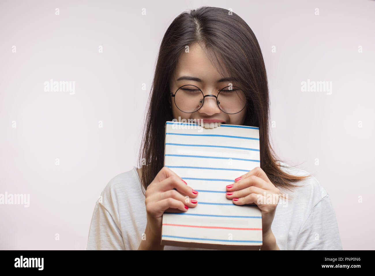 Lazy Asian student female biting a book, unwilling to study, isolated at studio. Stock Photo