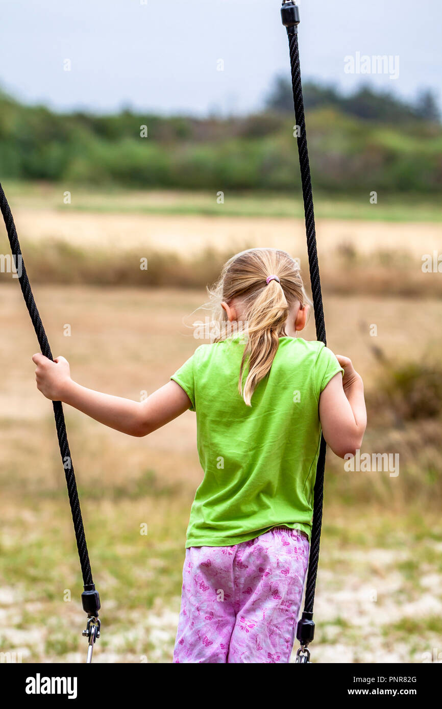 Little girl having fun standing on outdoor swing Stock Photo