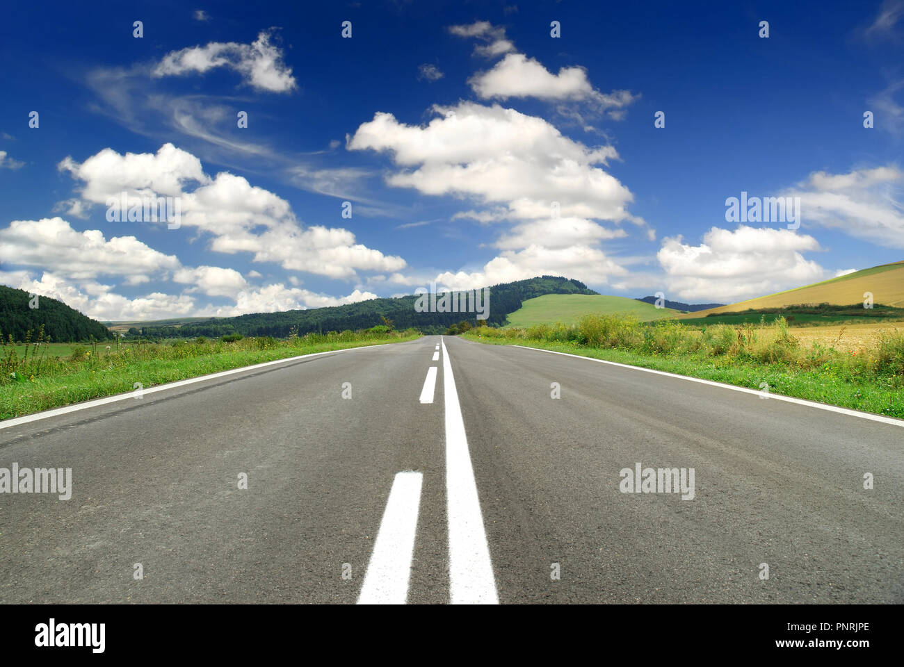 Road among green fields, blue sky and white clouds in the background ...