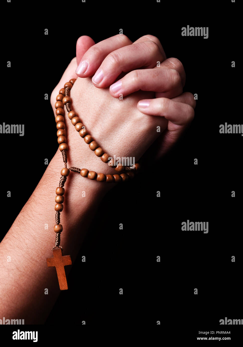 Female hands praying holding a beads rosary with a cross or Crucifix on black background. Woman with Christian Catholic religious faith. Profile or si Stock Photo