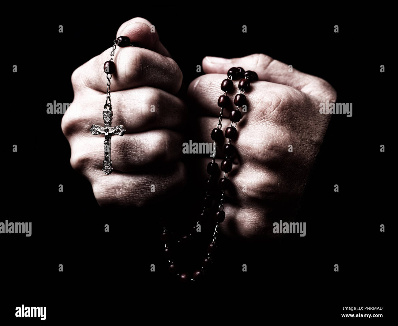 Female hands praying holding a rosary with Jesus Christ in the cross or Crucifix on black background. Woman with Christian Catholic religious faith Stock Photo