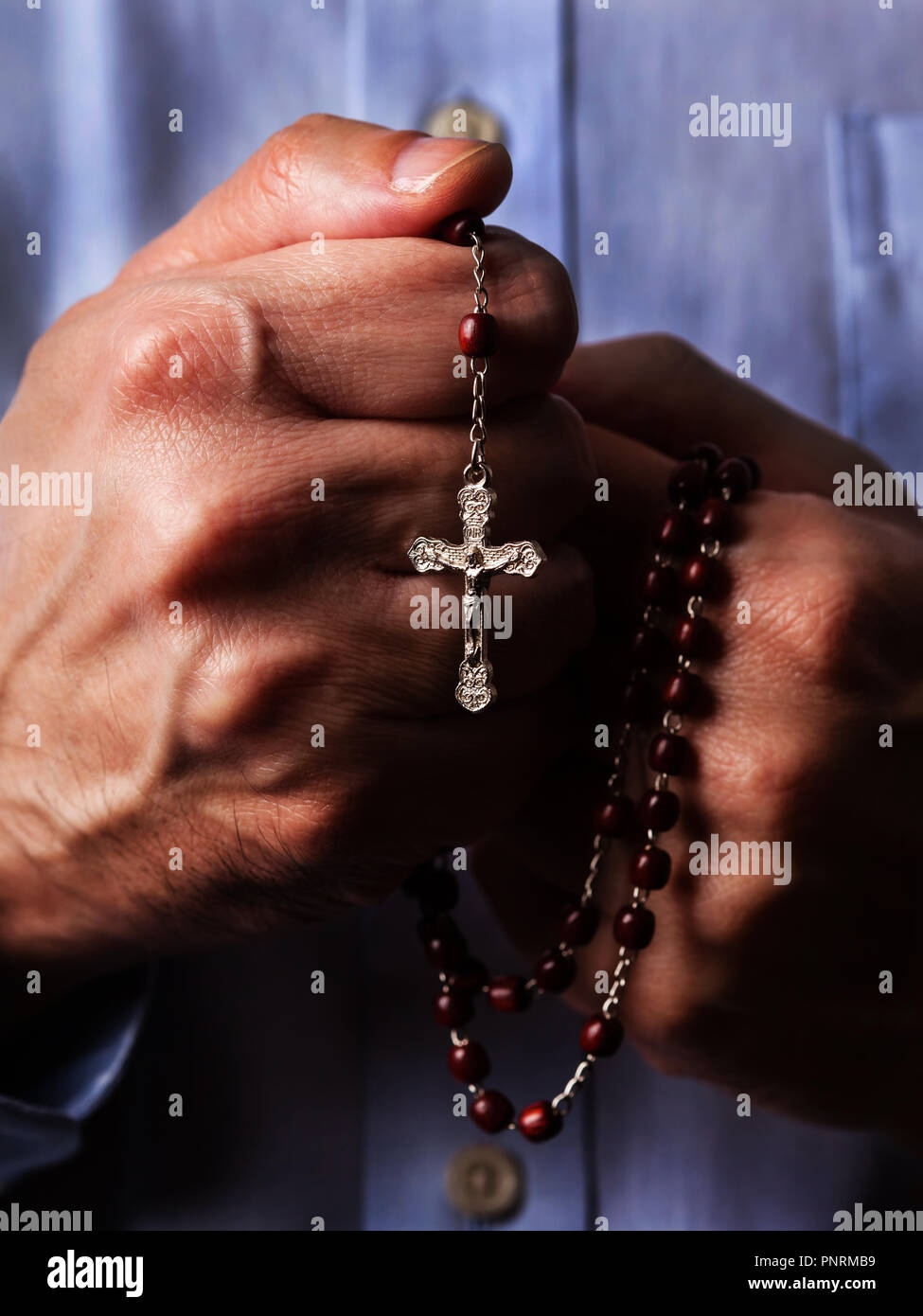 Male hands praying holding a beads rosary with Jesus Christ in the cross or Crucifix on black background. Mature man with Christian Catholic religious Stock Photo