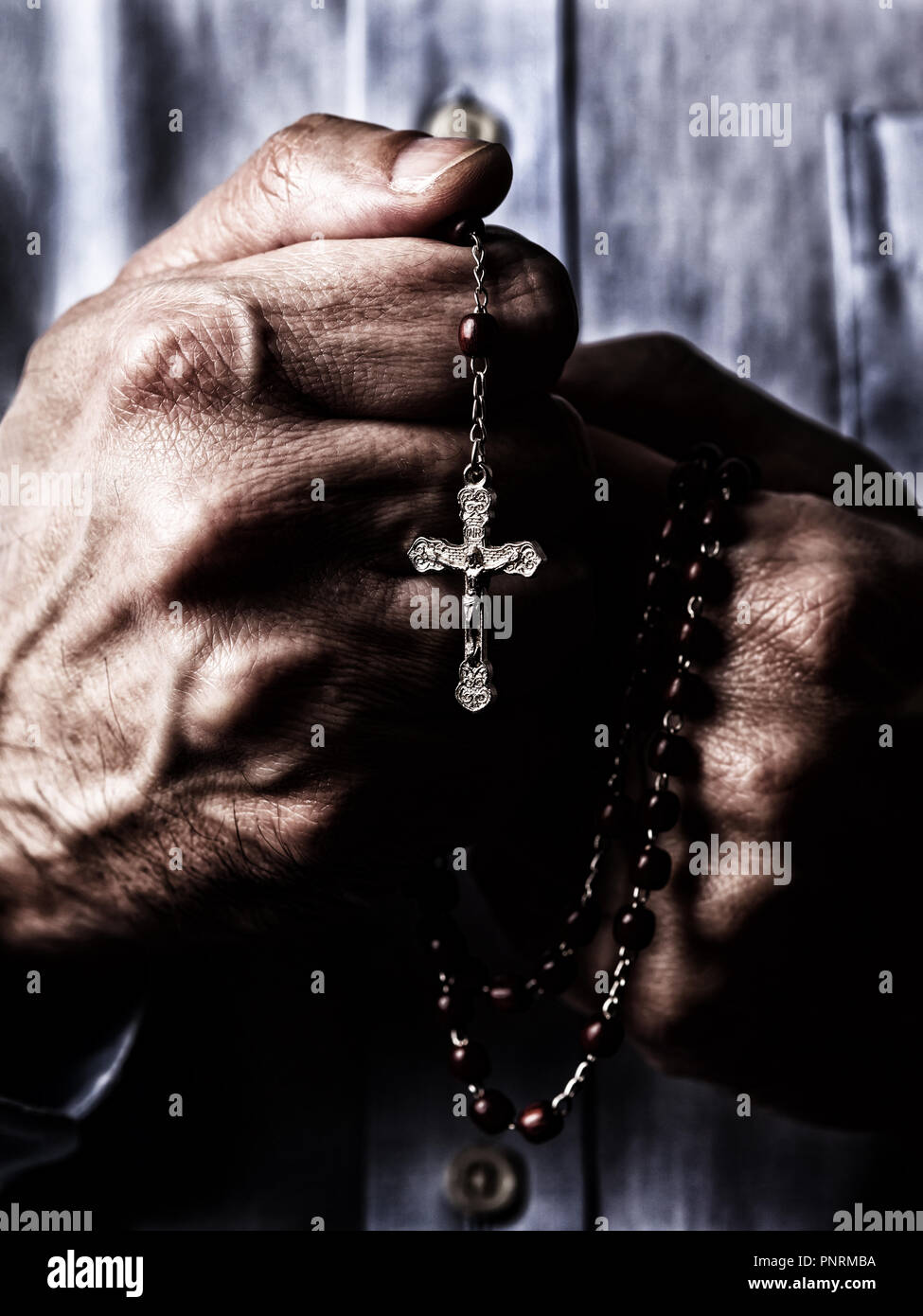 African American male hands praying holding a beads rosary with Jesus Christ in the cross or Crucifix on black background. Mature Afro American man wi Stock Photo