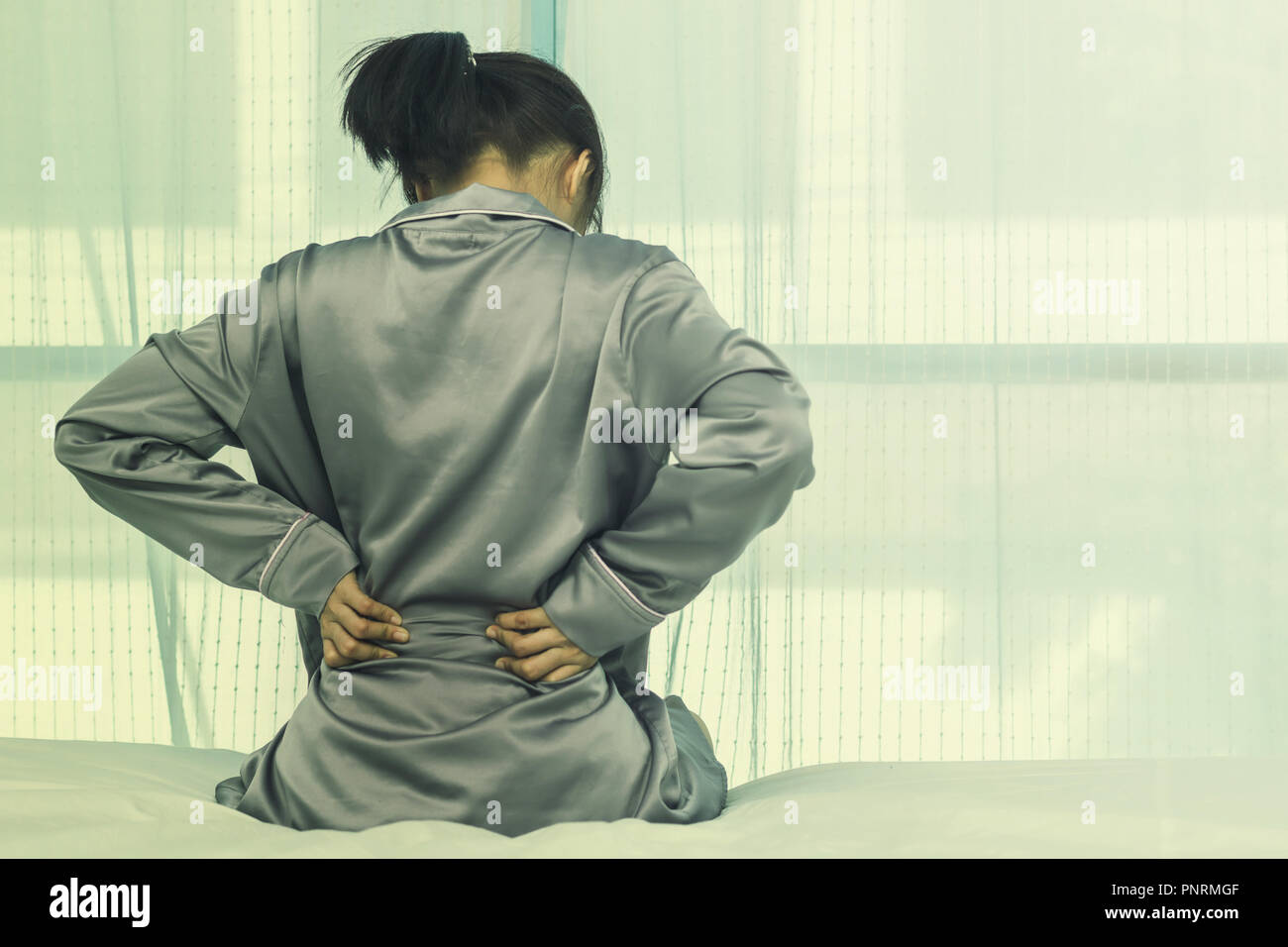 Asian woman back pain and sit on bed in bedroom in the morning Stock