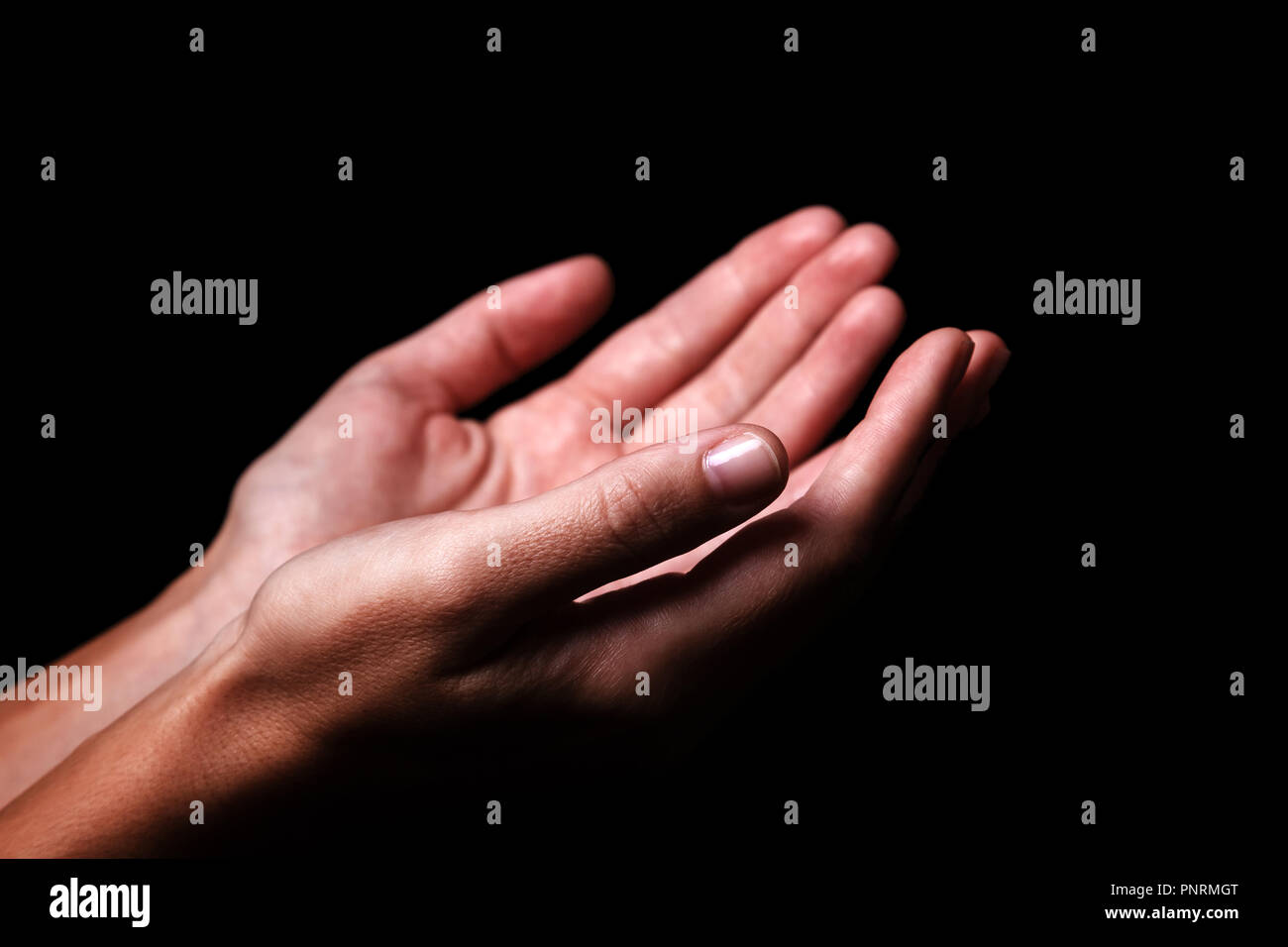 Female hands praying with palms up arms outstretched. Black background. Close up of woman hand. Concept for prayer, faith, religion, religious, worshi Stock Photo