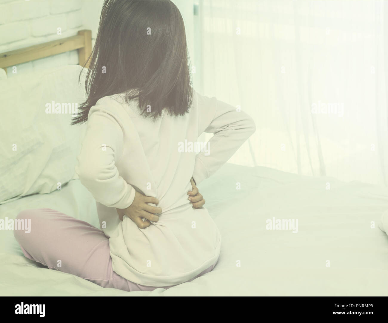 Asian woman back pain and sit on bed in bedroom in the morning.color