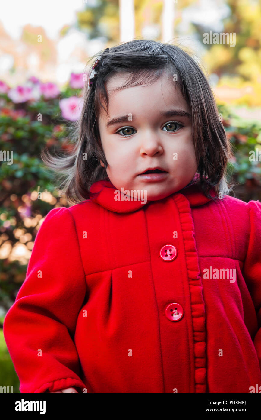 Cute, pretty, happy, smiling toddler baby girl, with a naughty playful smile with elegant red overcoat or long coat. Eighteen or 18 months old Stock Photo