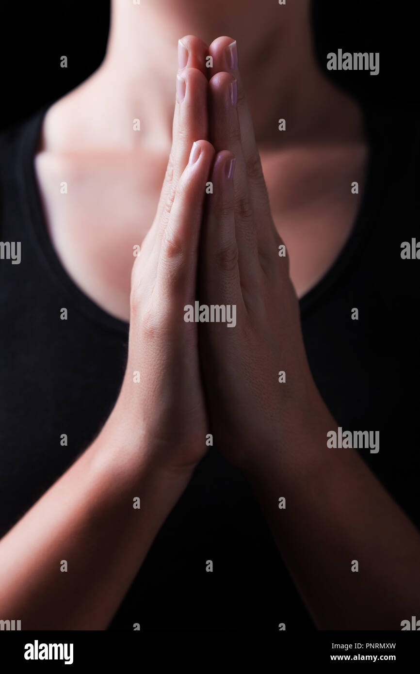Low key, close up of hands of a faithful woman praying, with hands folded and palms together in worship to god, on a black background. Concept for rel Stock Photo