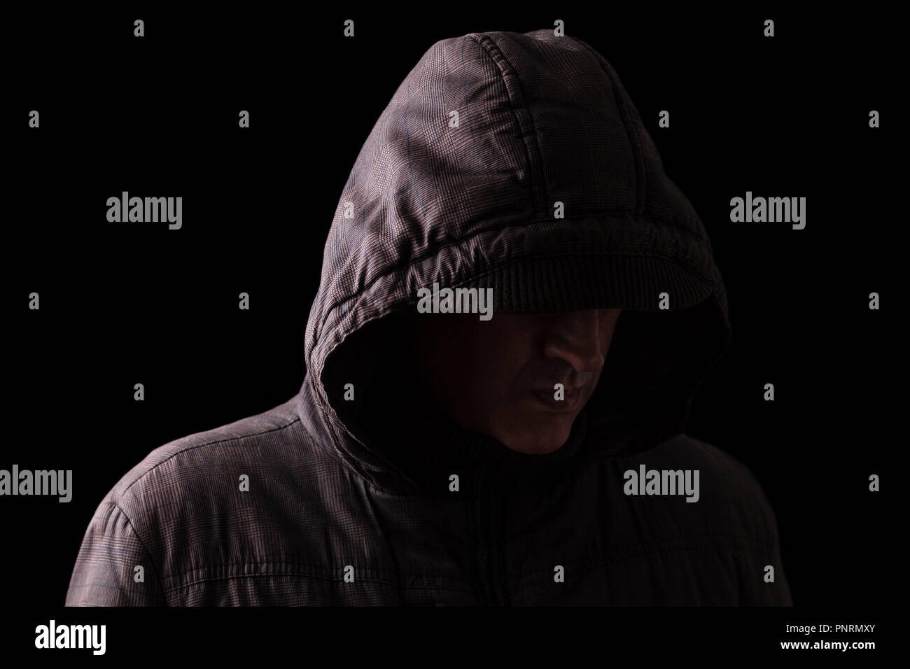 Scary and creepy caucasian or white man hiding in the shadows, with the face and identity hidden with the hood, and standing in the darkness. Low key, Stock Photo