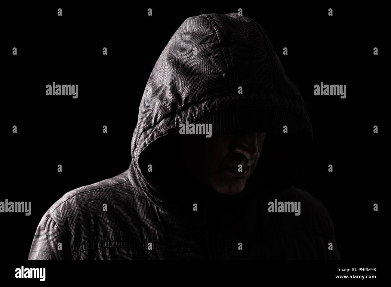 Scary and creepy caucasian or white man hiding in the shadows, with the face and identity hidden with the hood, and standing in the darkness. Low key, Stock Photo