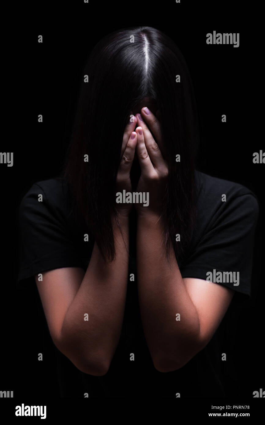 Emotional woman crying and covering the face with the hands hiding the tears, on a black or dark background. Concept for victim depression pain grief Stock Photo