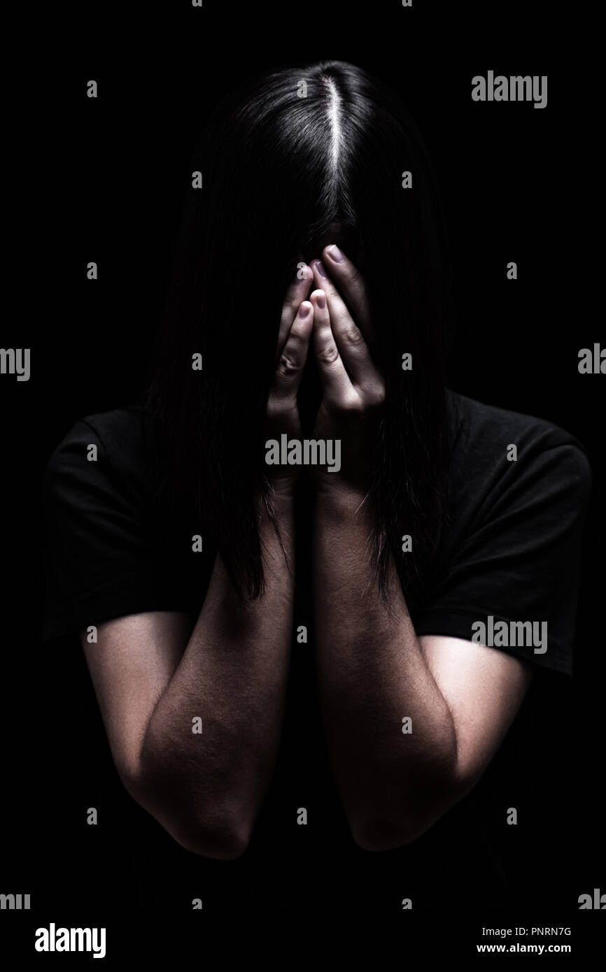 Emotional woman crying and covering the face with the hands hiding the tears, on a black or dark background. Concept for victim depression pain grief Stock Photo