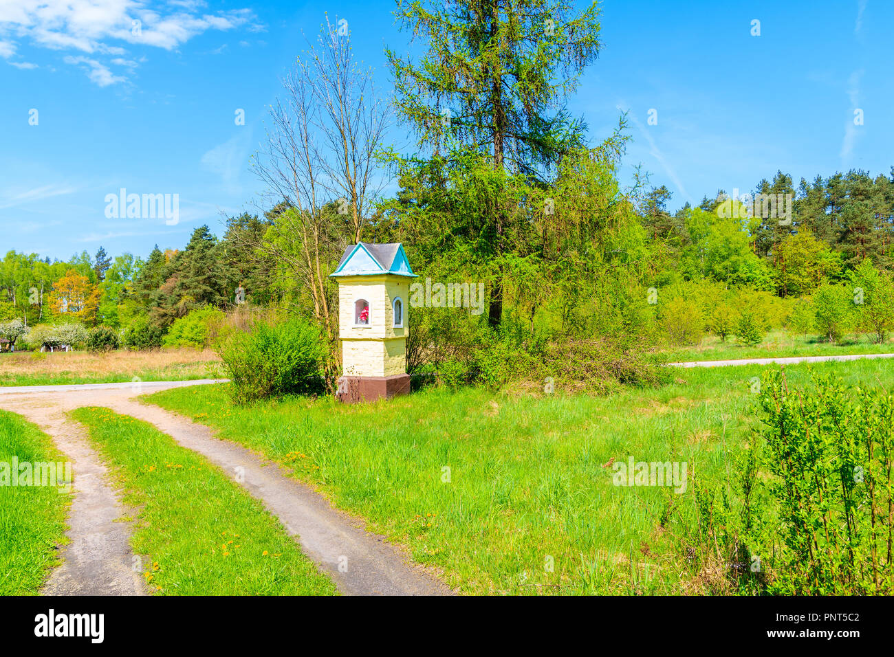 Small chapel on side of rural road with green trees near Krakow city during spring season, Poland Stock Photo