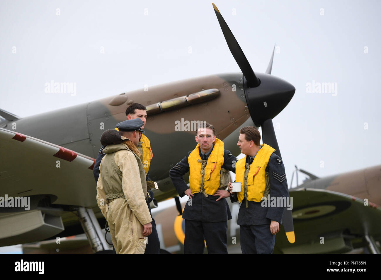 Historical reenactment members from Spirit of Britain (left to right) Darren Porter, Max Birkett, Jack Holt and Alex Hills with a Supermarine Spitfire on the flight line before the Battle of Britain Air Show at the Imperial War Museum in Duxford, Cambridgeshire. Stock Photo