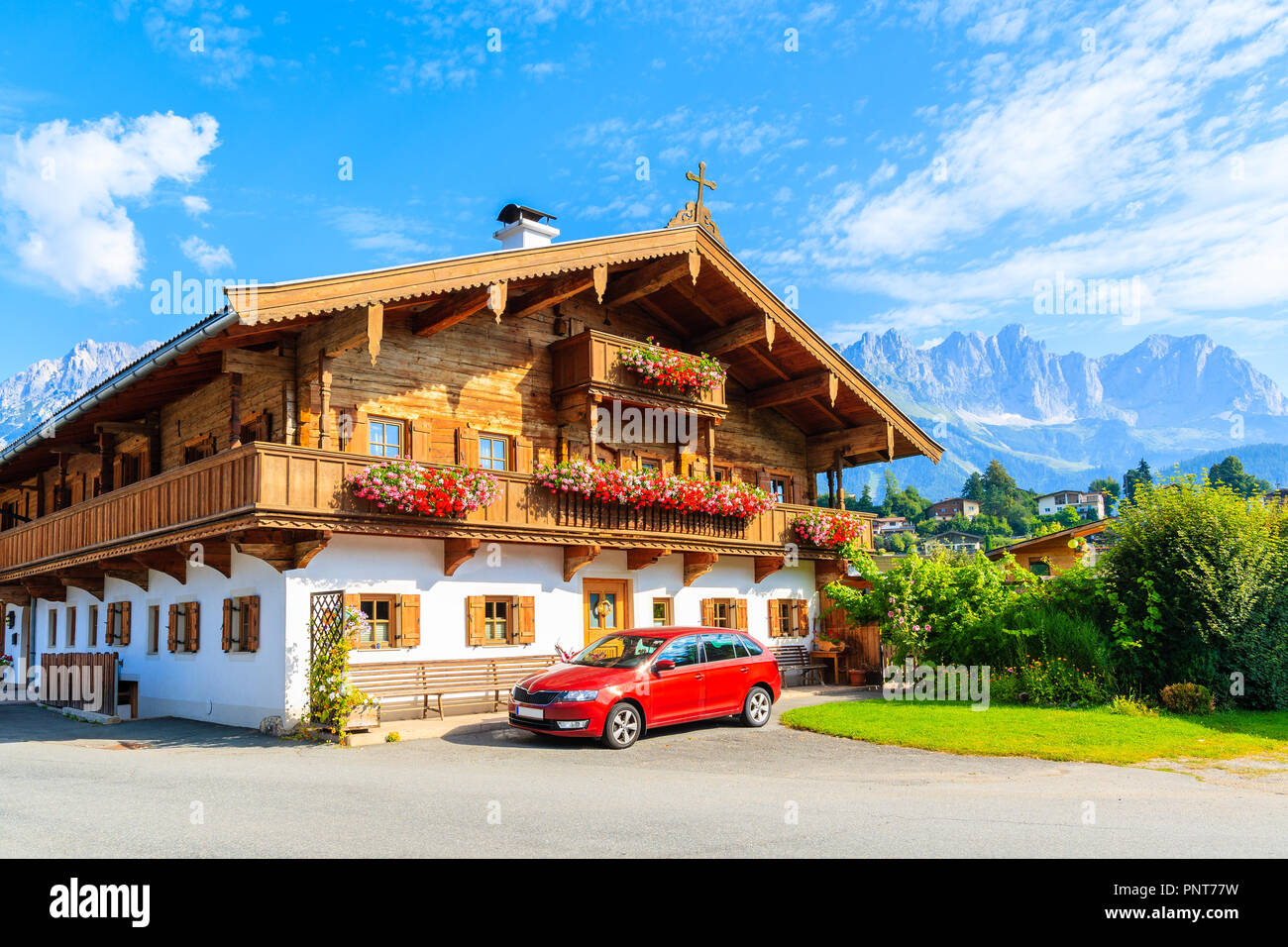 Traditional wooden alpine house decorated with flowers in Going am Wilden Kaiser mountain village on sunny summer day, Tyrol, Austria Stock Photo