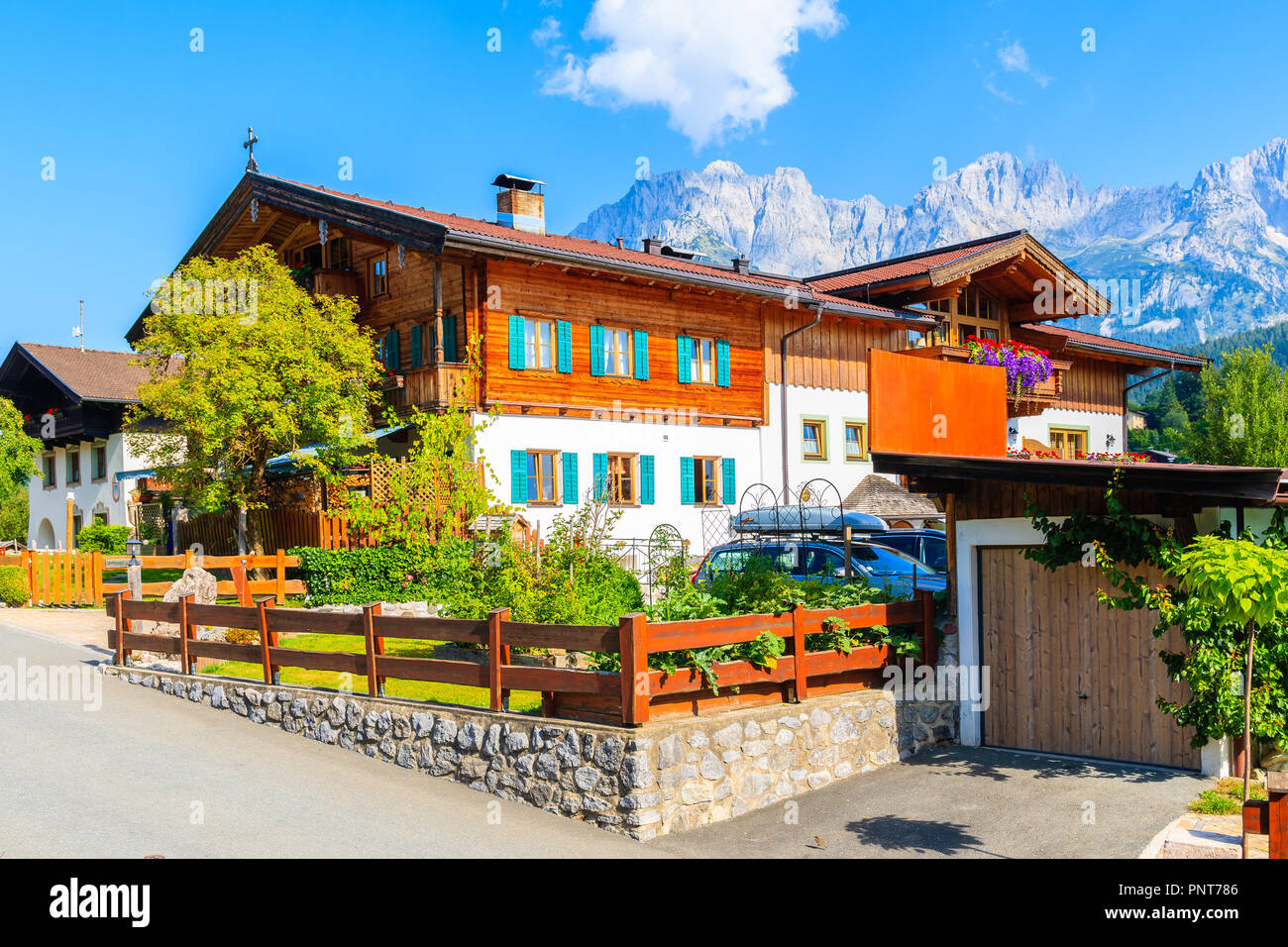 Traditional wooden alpine house decorated with flowers on green meadow in Going am Wilden Kaiser mountain village on sunny summer day, Tyrol, Austria Stock Photo