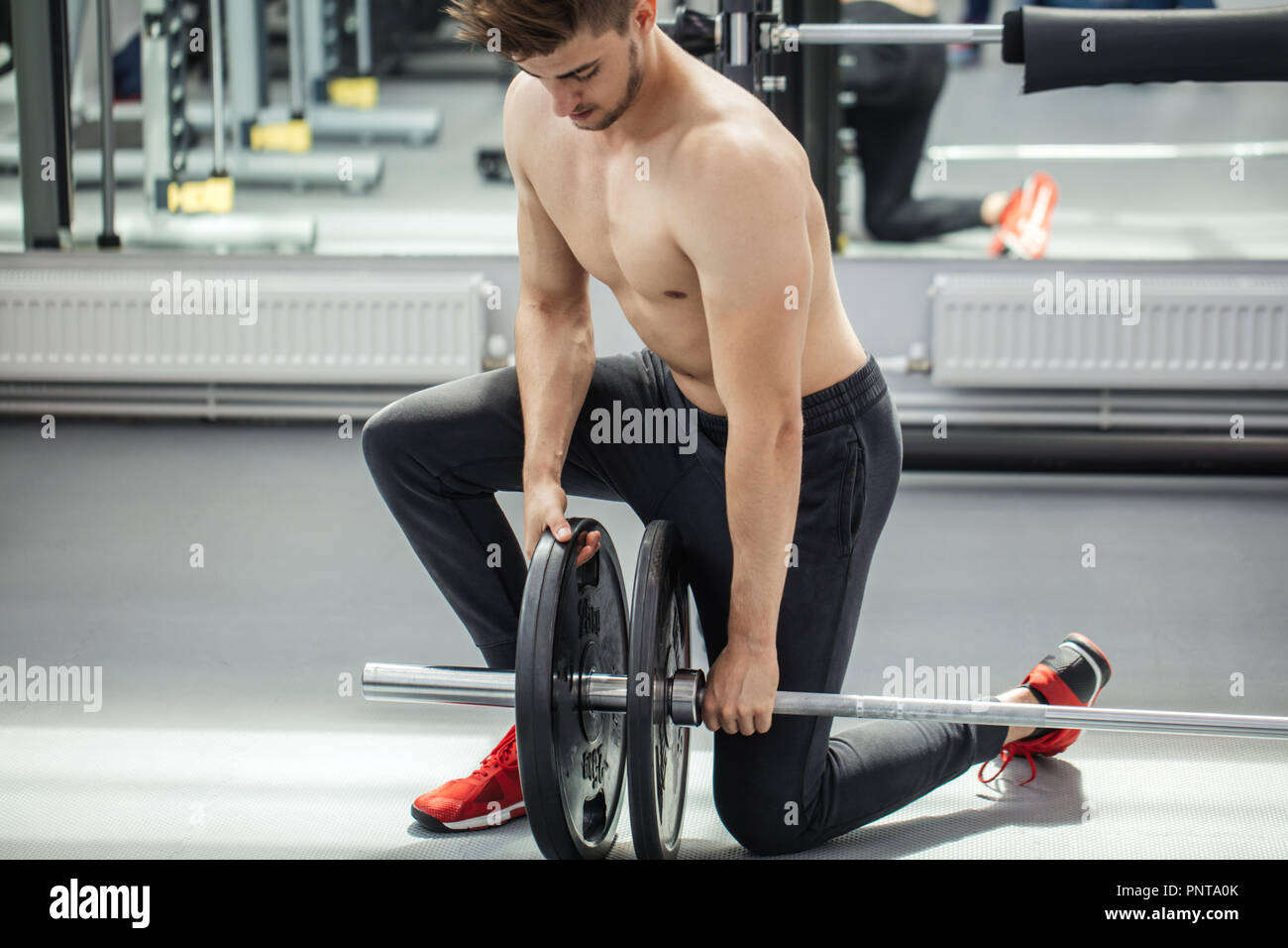 Muscular man putting heavy plates on barbell during workout in gym