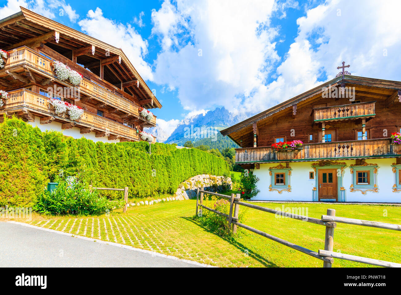 Traditional wooden alpine houses decorated with flowers on green meadow in Going am Wilden Kaiser mountain village on sunny summer day, Tyrol, Austria Stock Photo