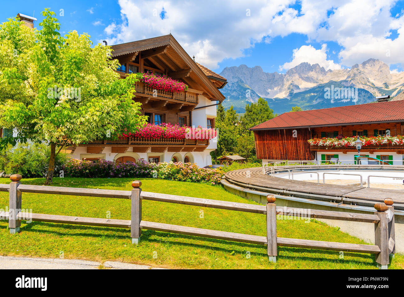 Typical wooden alpine house decorated with flowers on green meadow in Going am Wilden Kaiser village on sunny summer day, Tyrol, Austria Stock Photo